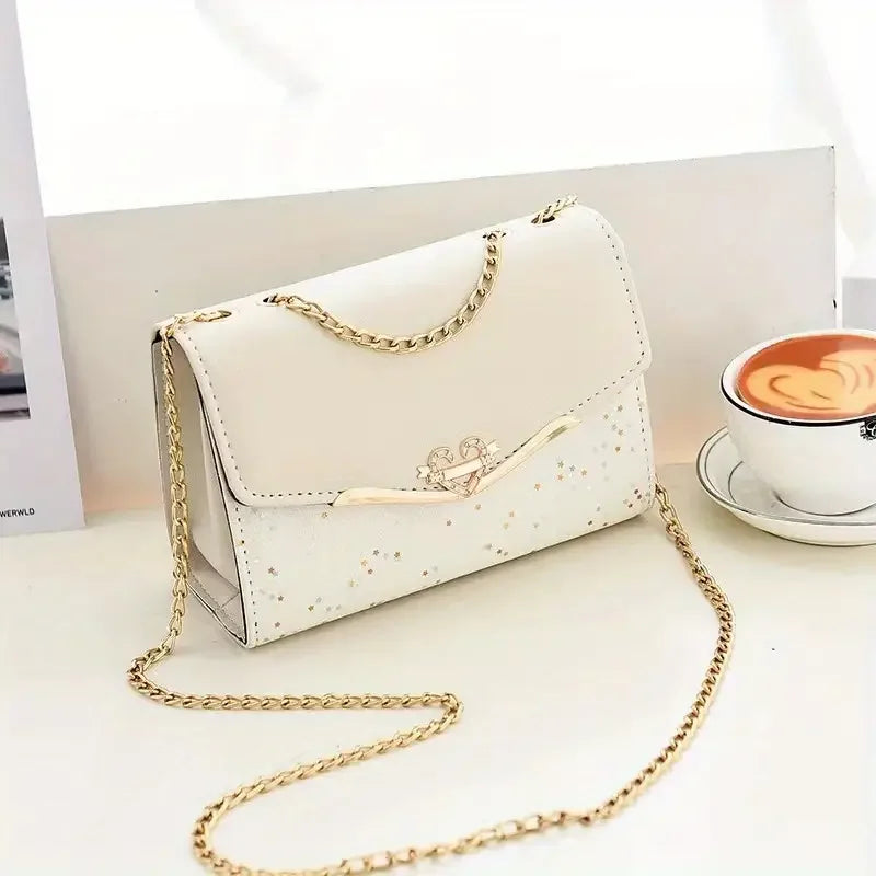 Cream crossbody purse with gold chain, star accents, and cappuccino on white table