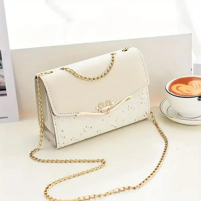 Cream crossbody purse with gold chain, star accents, and cappuccino on white table