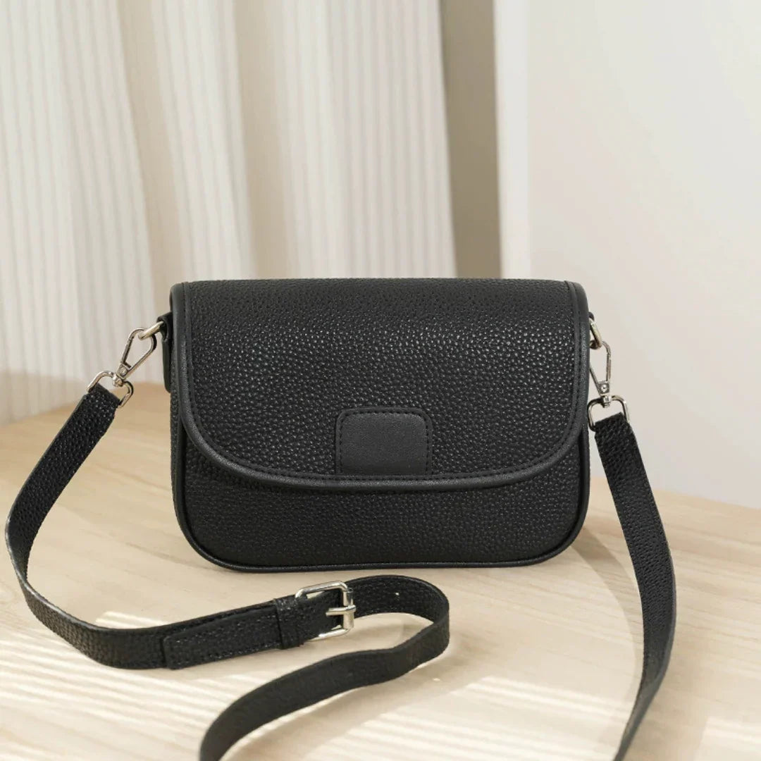 Black textured crossbody bag with adjustable strap on light wood table in bright room