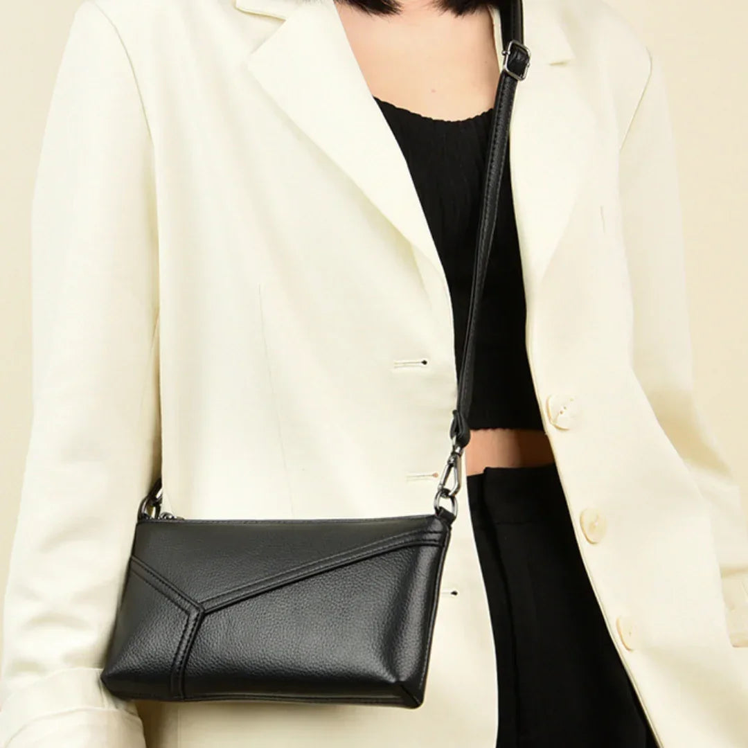 Woman in white blazer carries a black leather crossbody bag with geometric stitching