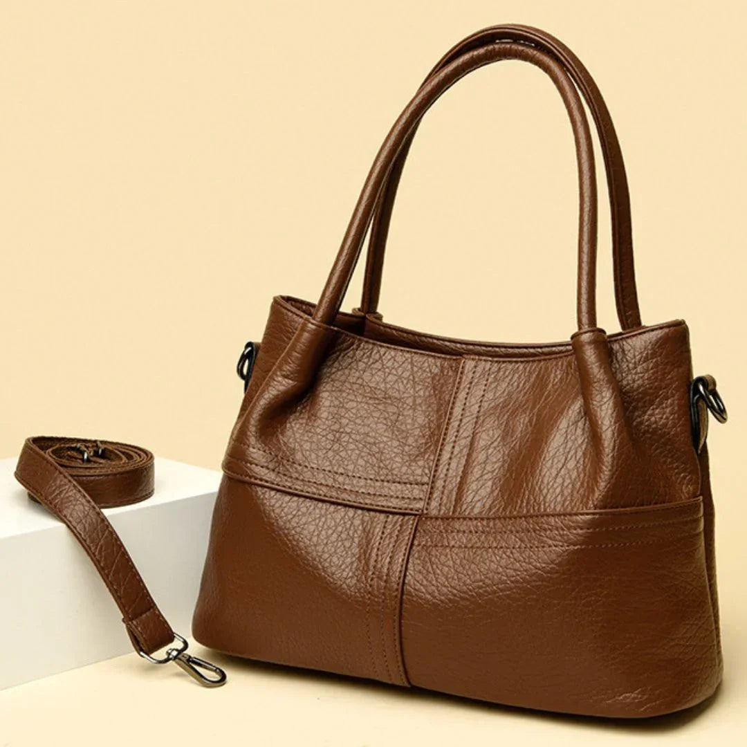 Brown leather handbag with double handles and detachable strap on beige background