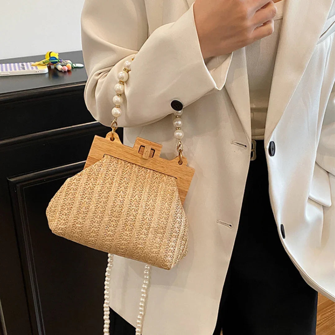 Woman in cream blazer holding woven straw handbag with pearl handle