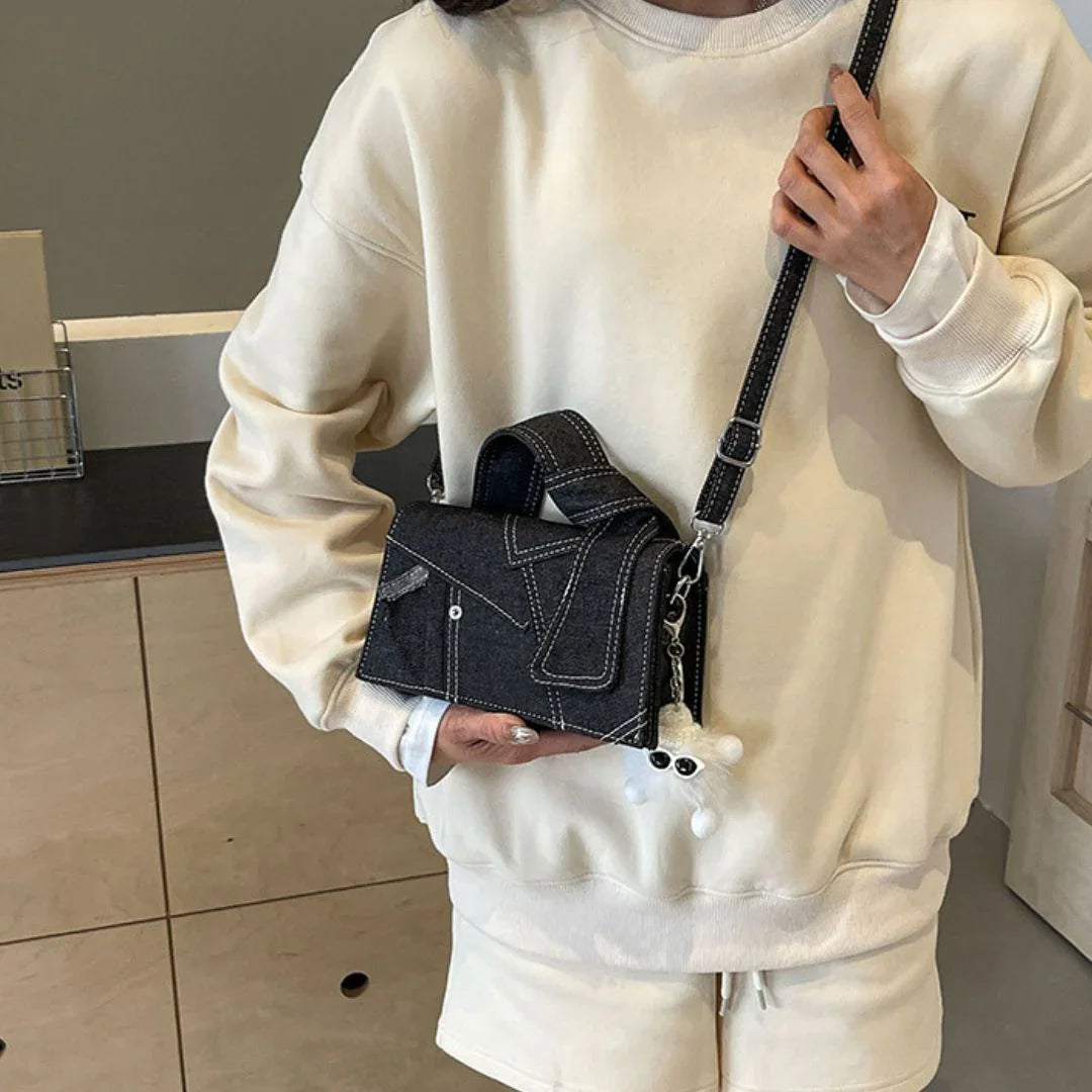 Woman in cream sweatshirt with denim crossbody bag featuring white plush keychain