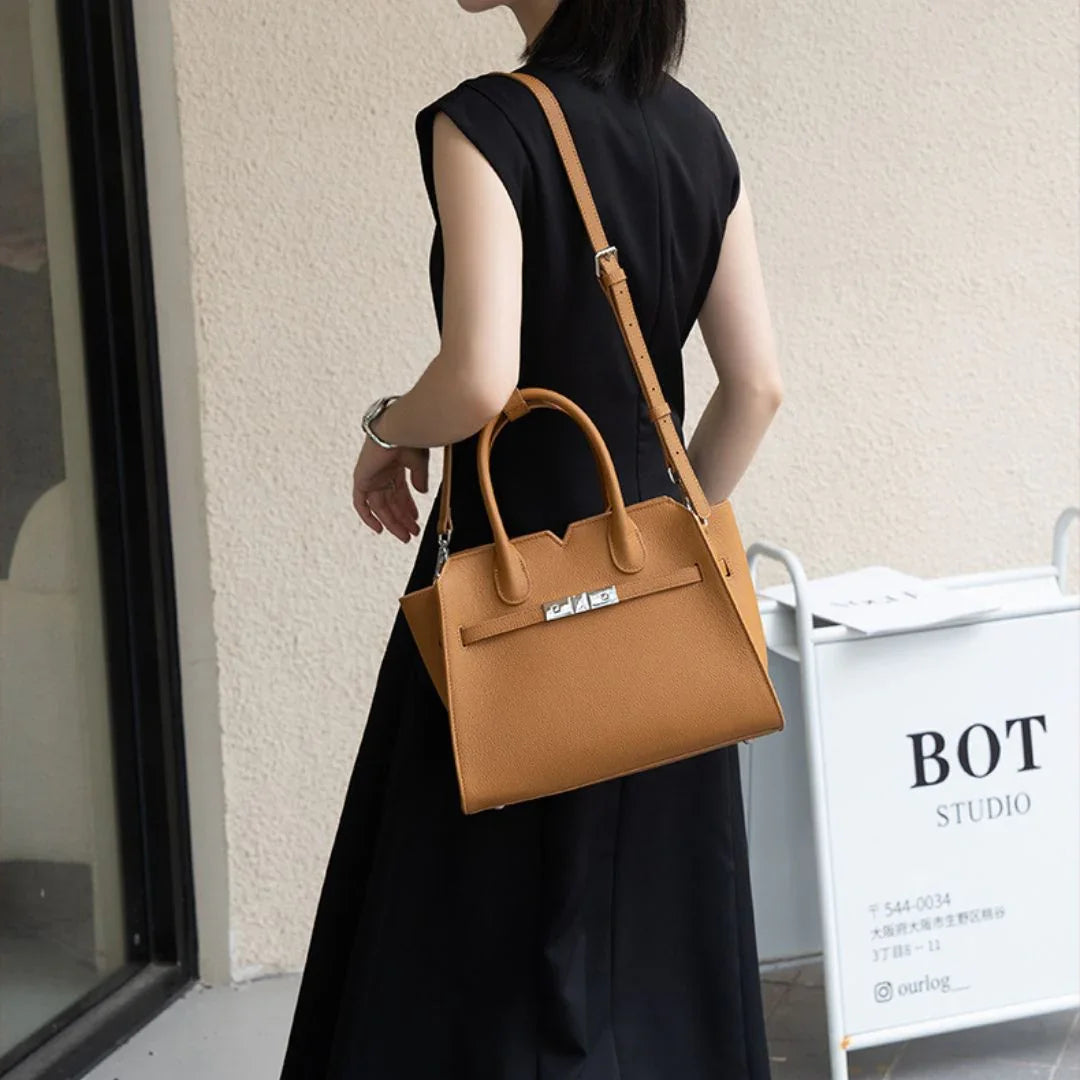 Woman in black dress carrying a tan leather handbag with shoulder strap near BOT Studio sign