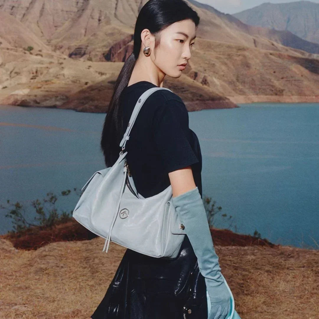 Woman in black shirt and blue gloves with light blue handbag by a mountain lake