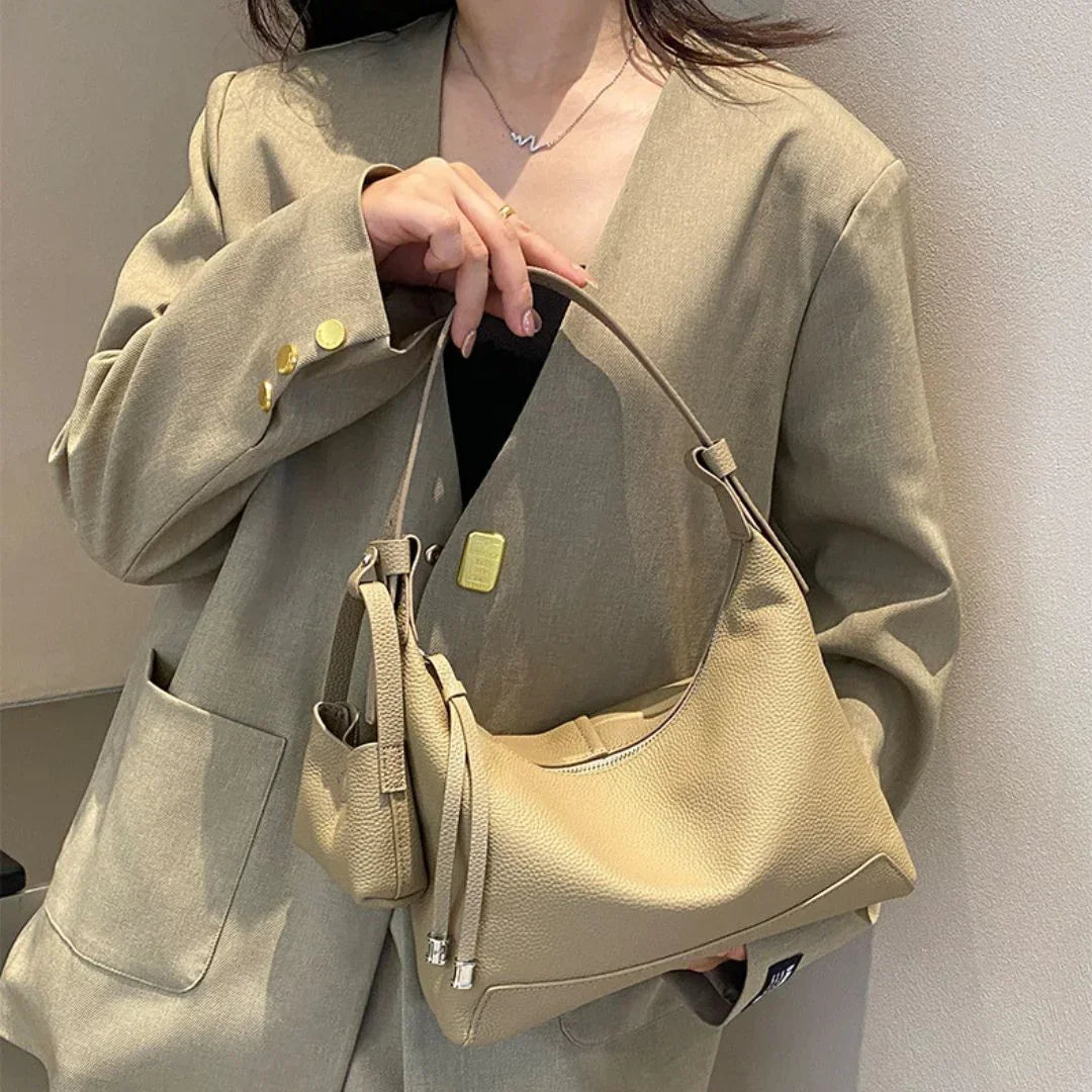 Woman in beige blazer holding a stylish beige leather shoulder bag with gold accents