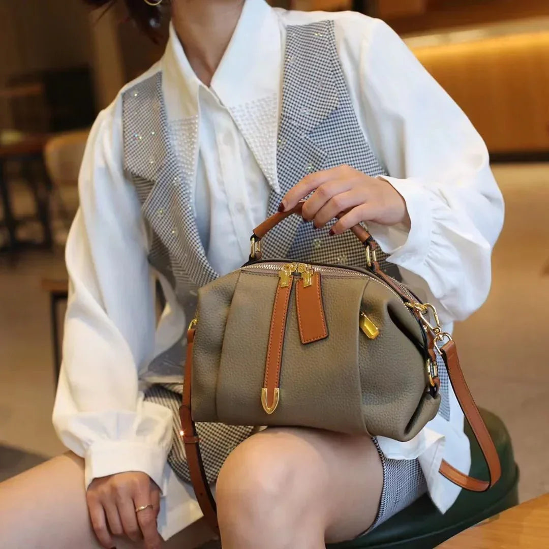 Woman in white blouse with gray vest holding a stylish taupe leather handbag with brown straps