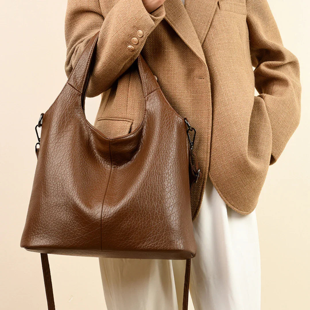 Woman in tan blazer holding large brown leather tote bag with shoulder strap