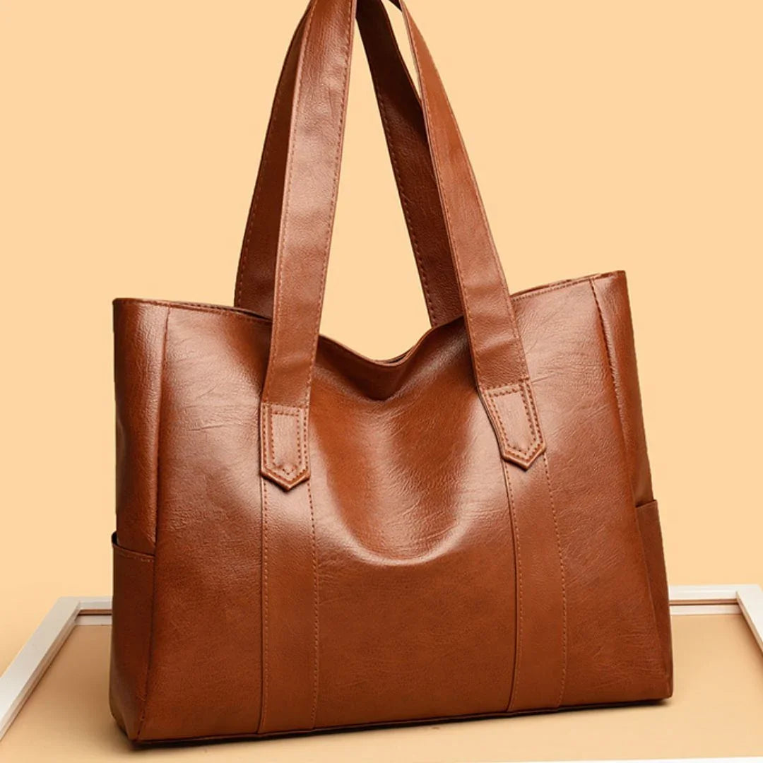 Brown leather tote bag with double handles on peach background