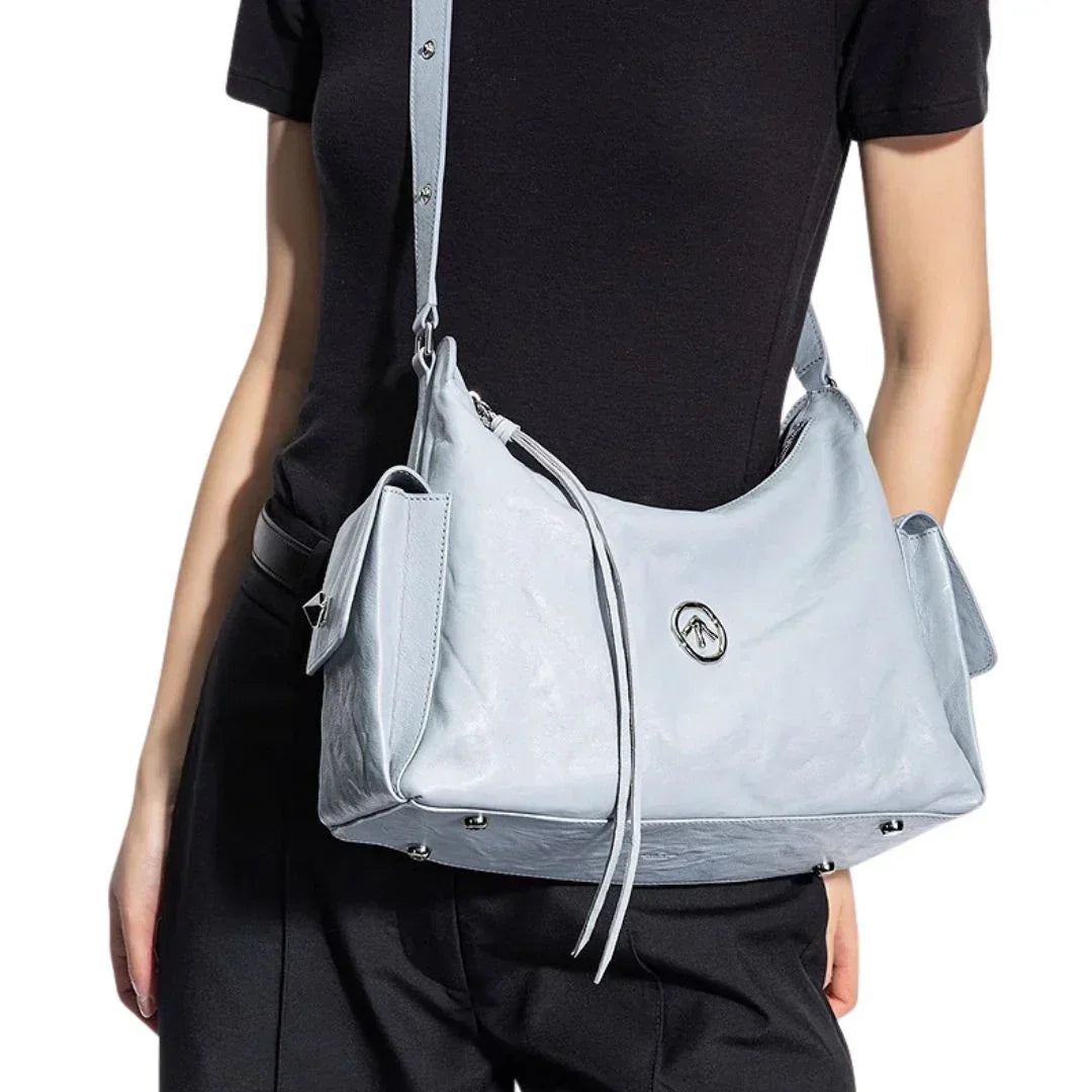 Light blue leather shoulder bag with side pockets and silver logo, worn by woman in black top