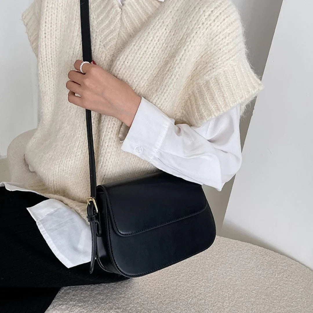 Woman in cream knit vest and white shirt with black leather crossbody bag