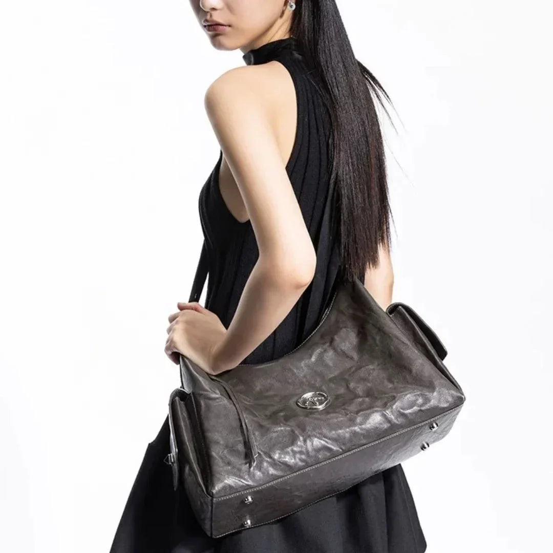 Woman in black dress carrying large metallic leather shoulder bag on white background