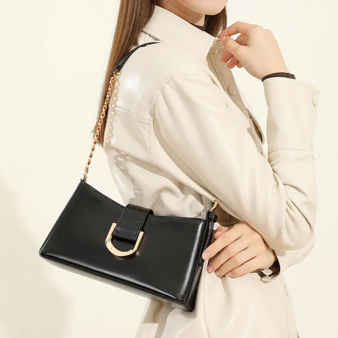 Woman in beige jacket holding black leather shoulder bag with gold chain strap