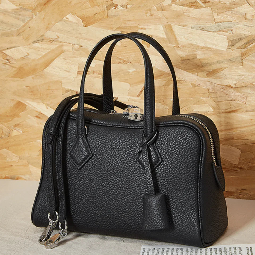 Black leather handbag with silver hardware and top handles on a neutral background