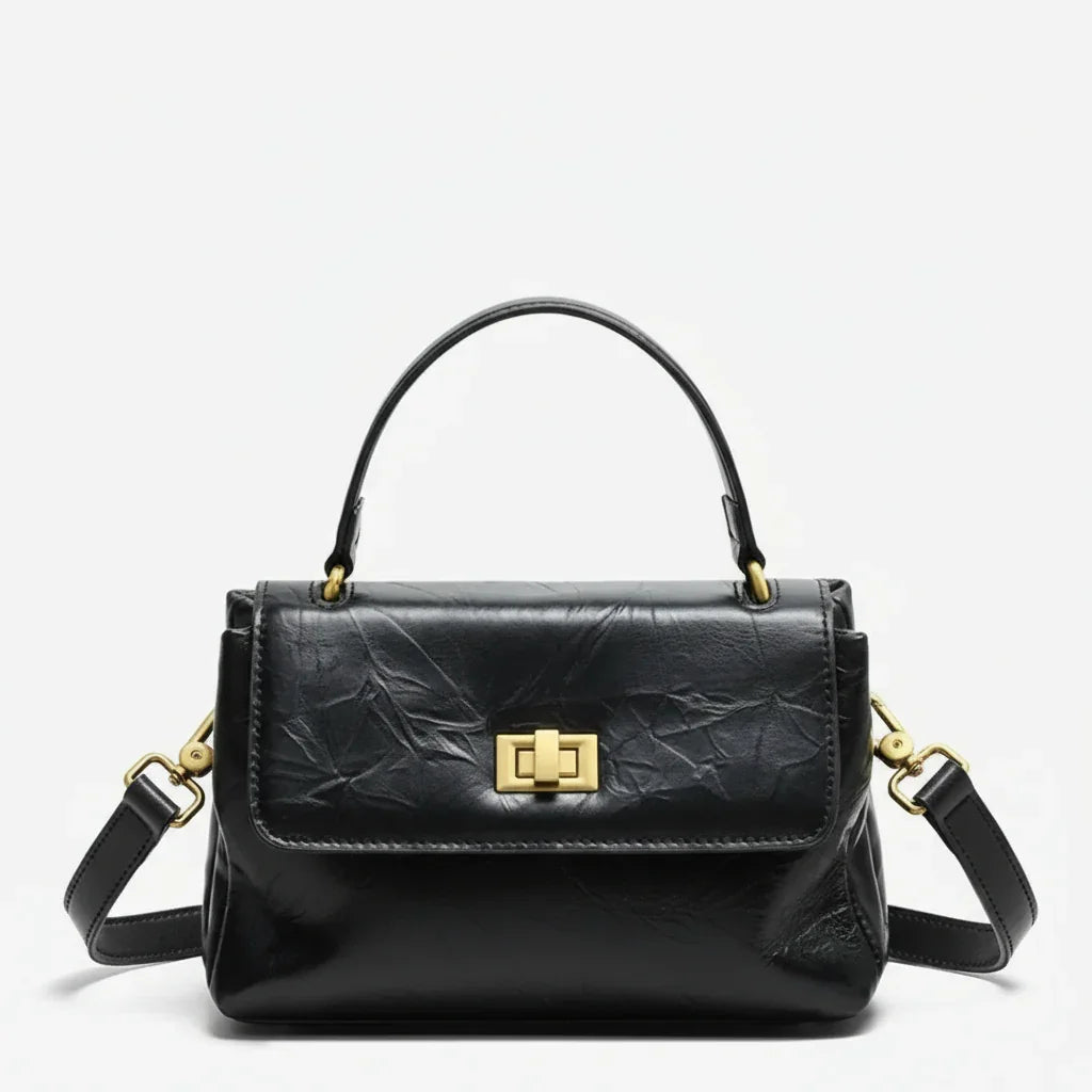 Black leather handbag with gold hardware and top handle on a white background