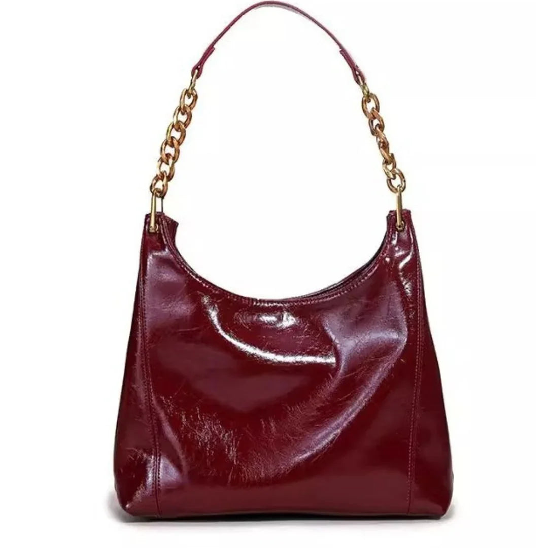 Glossy burgundy leather handbag with gold chain strap on white background