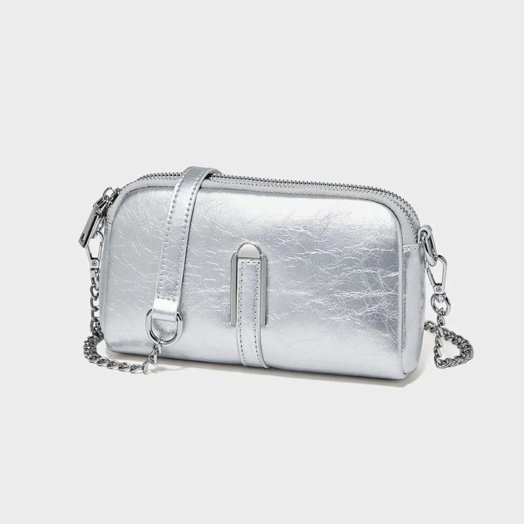 Metallic silver crossbody bag with chain strap and zipper on a plain light background