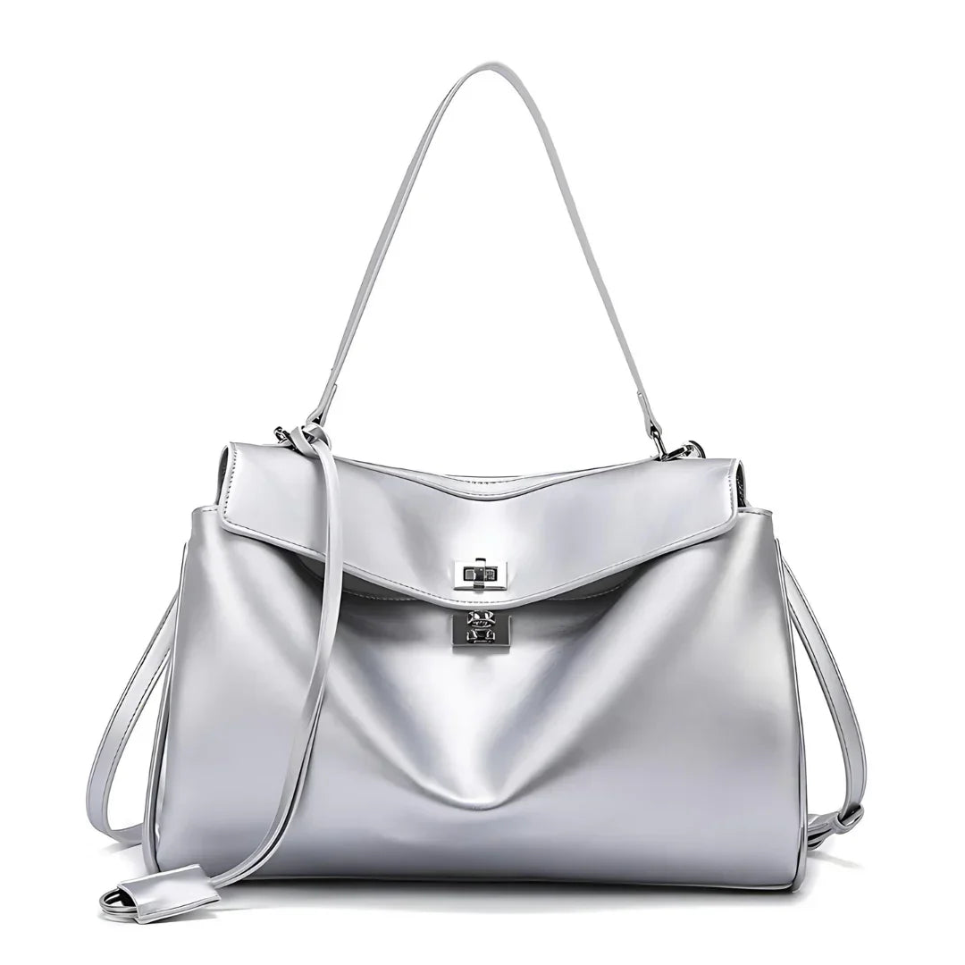 Silver leather handbag with shoulder strap, top flap, and turn-lock closure on white background.