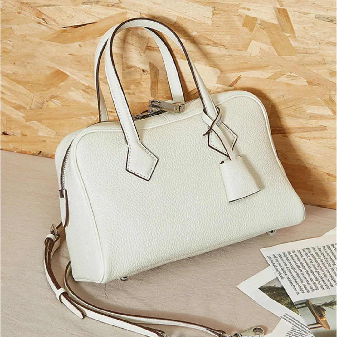 White leather handbag with top handles and a detachable strap on a beige surface