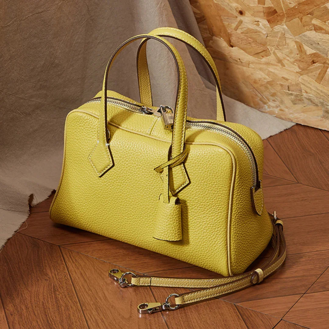 Yellow leather handbag with textured surface and detachable strap on a wooden floor