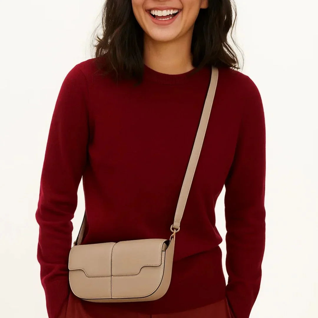 Woman in red sweater wearing beige crossbody leather bag, smiling against plain background