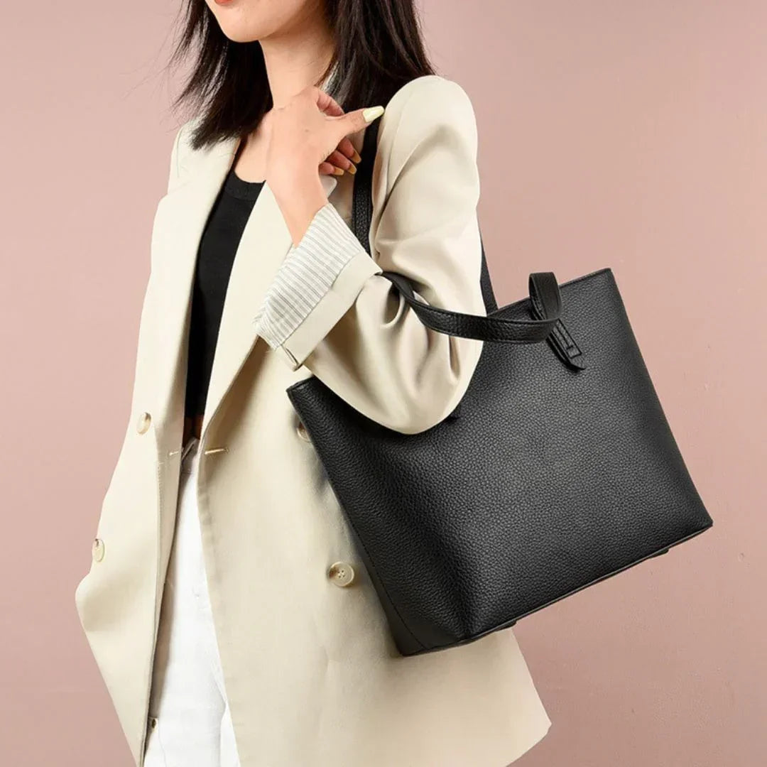 Woman in beige blazer with black leather tote bag against pink background