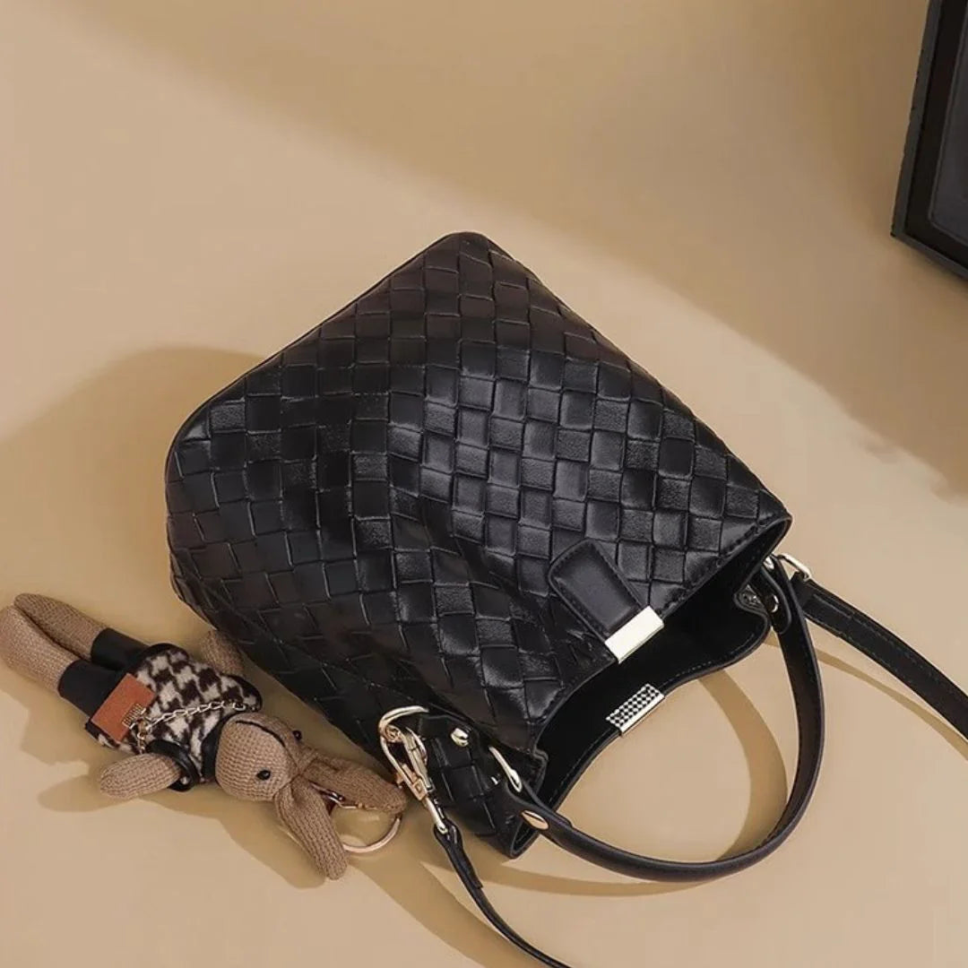 Woven black leather handbag with teddy bear keychain on beige background