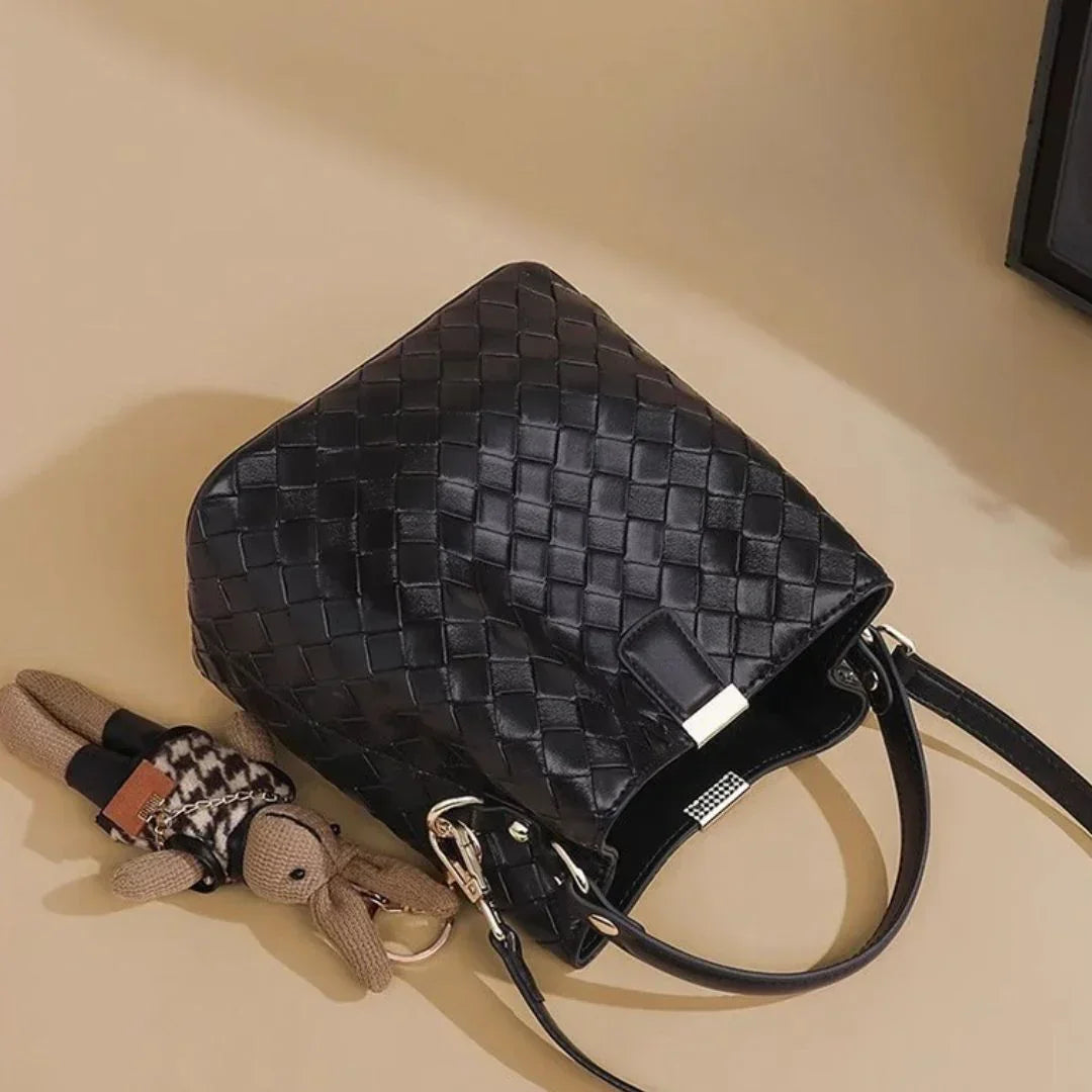 Woven black leather handbag with teddy bear keychain on beige background