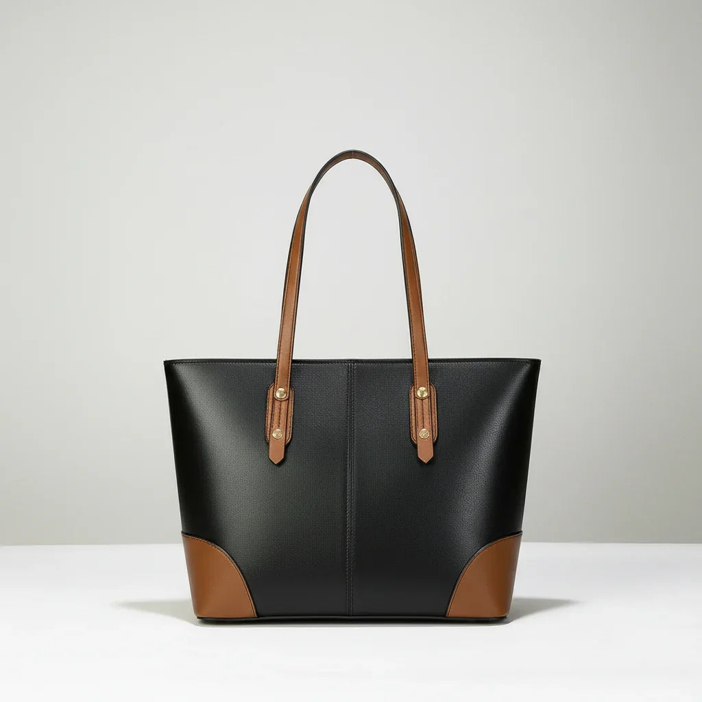 Black leather tote bag with brown handles and corners on a white surface