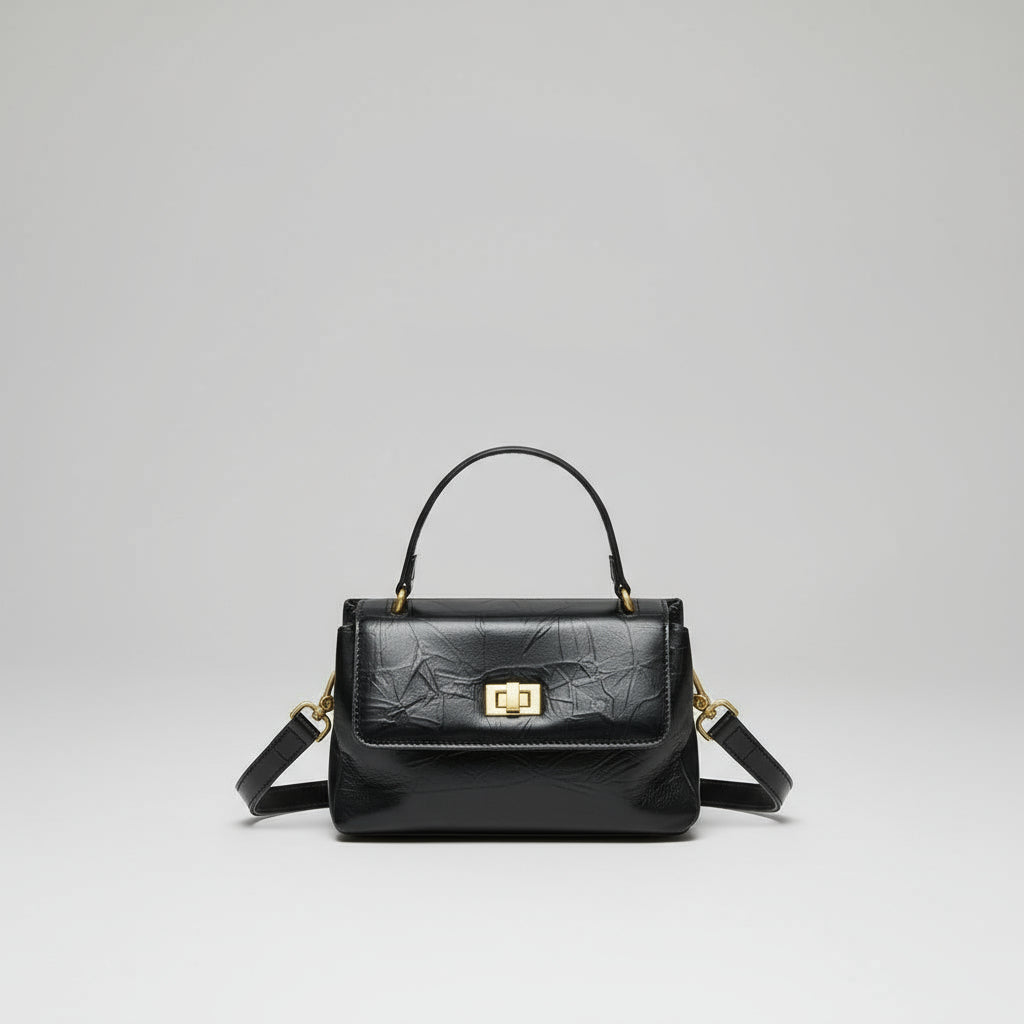 Black leather handbag with top handle, gold clasp, and detachable shoulder strap on white background