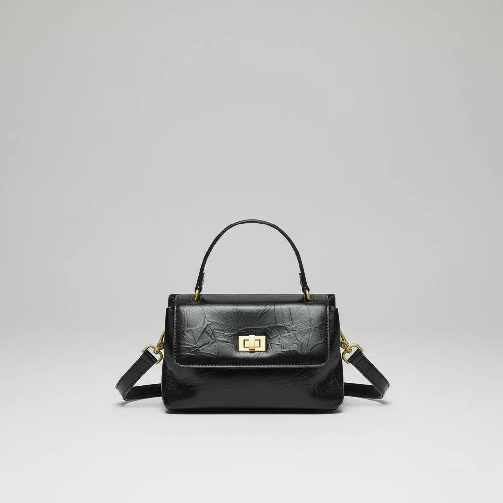 Black leather handbag with top handle, gold clasp, and detachable shoulder strap on white background