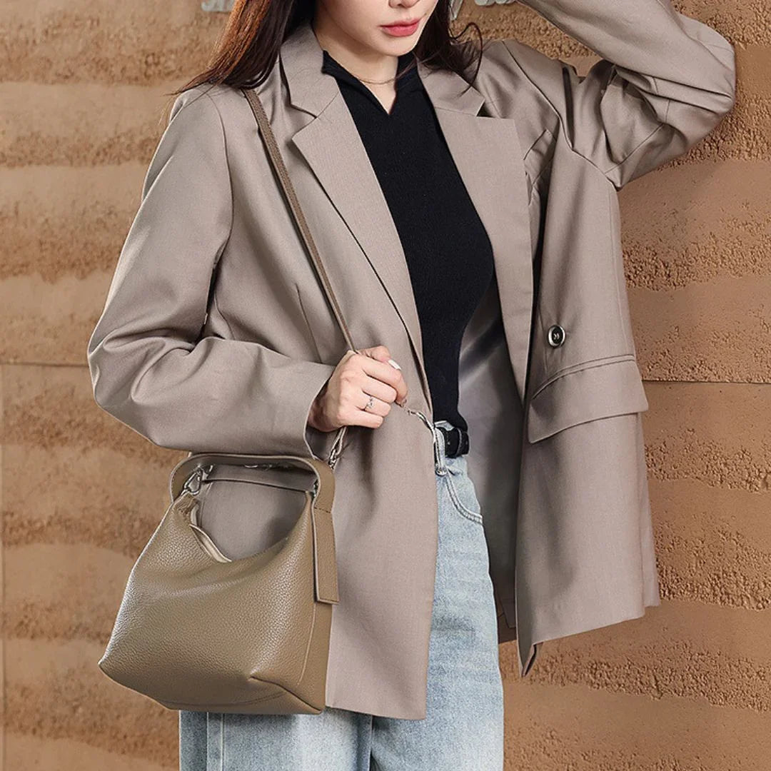 Woman wearing beige blazer, black top, light jeans and carrying taupe leather shoulder bag