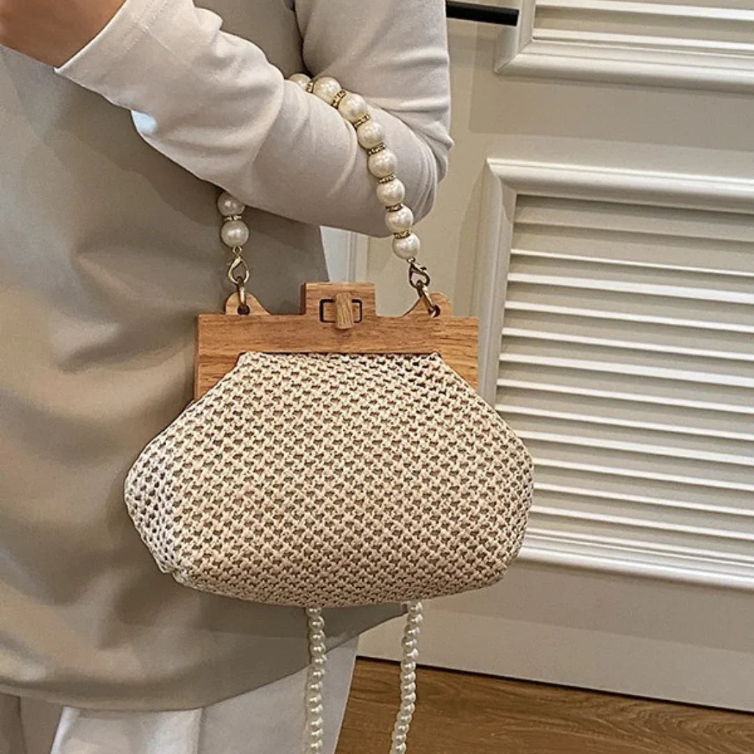 Boho woven clutch purse with wooden frame and pearl handle, held by person indoors