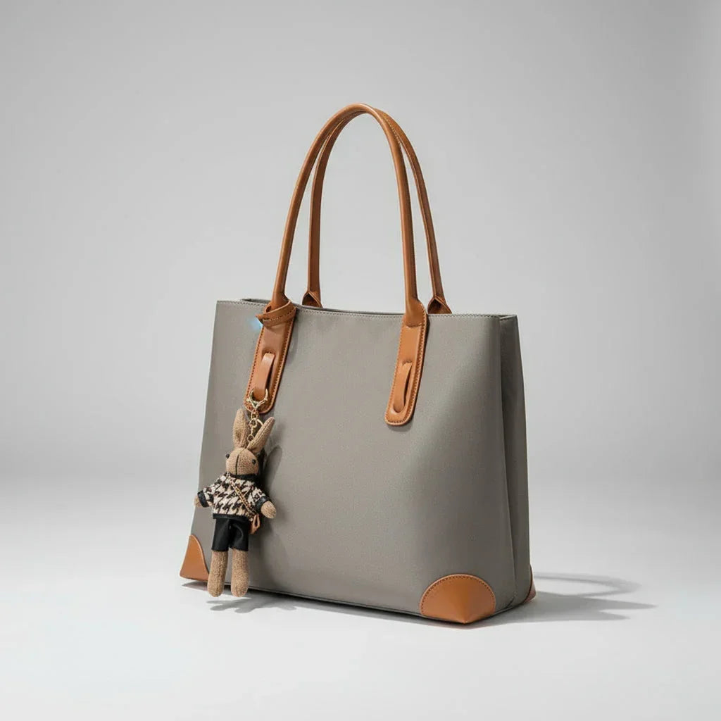 Grey tote bag with brown leather handles and bunny keychain, minimalist background