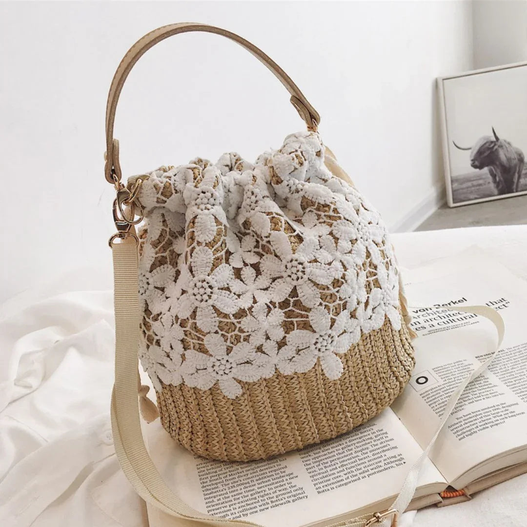 Straw crochet bucket bag with white floral lace, displayed on a bed with an open magazine.