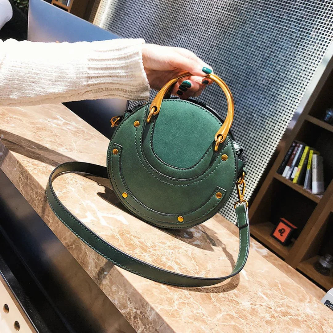 Green round handbag with gold hardware and top handle on marble table