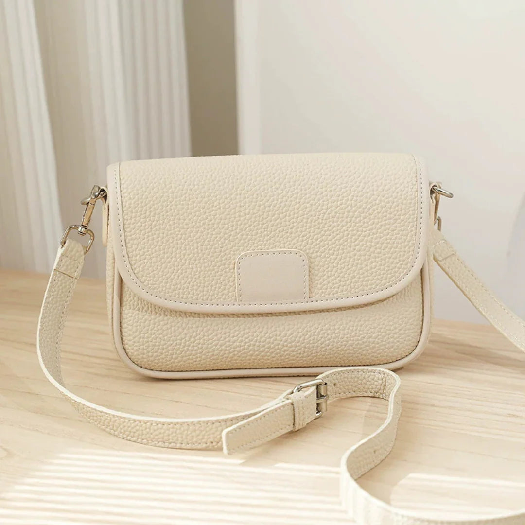 Beige textured leather crossbody bag on wooden table in natural light
