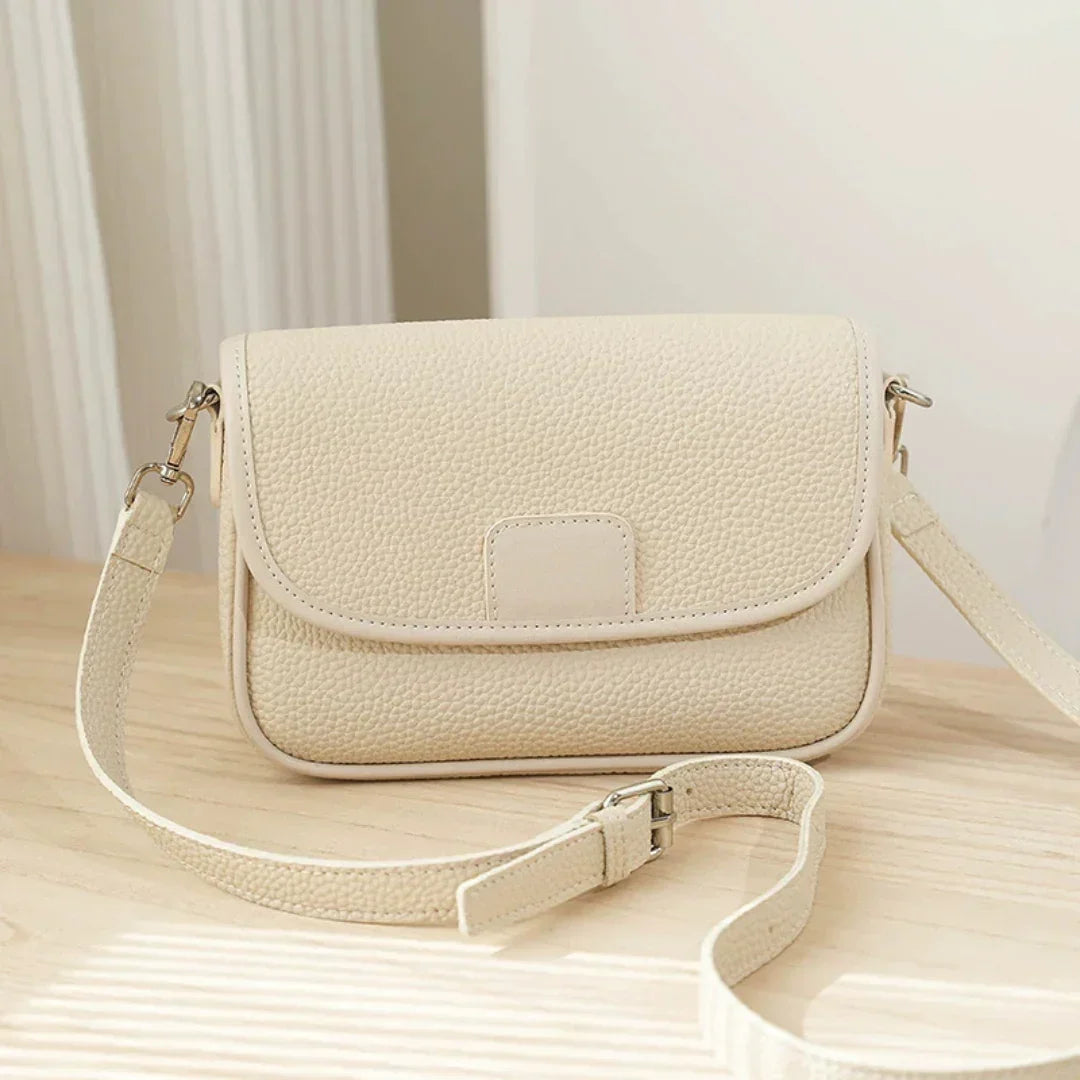 Beige textured leather crossbody bag on wooden table in natural light