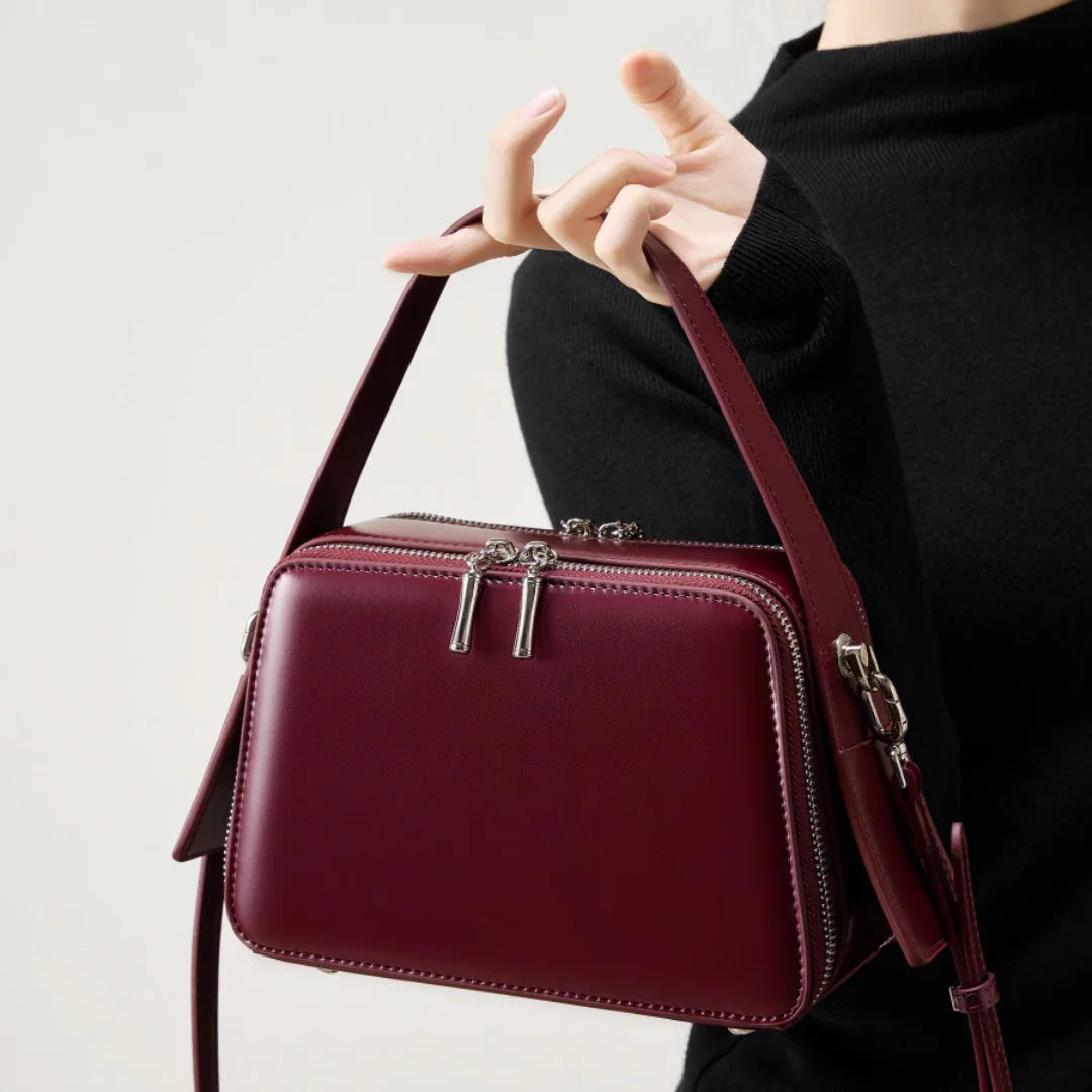 Woman in black sweater holding burgundy leather crossbody bag with silver zippers