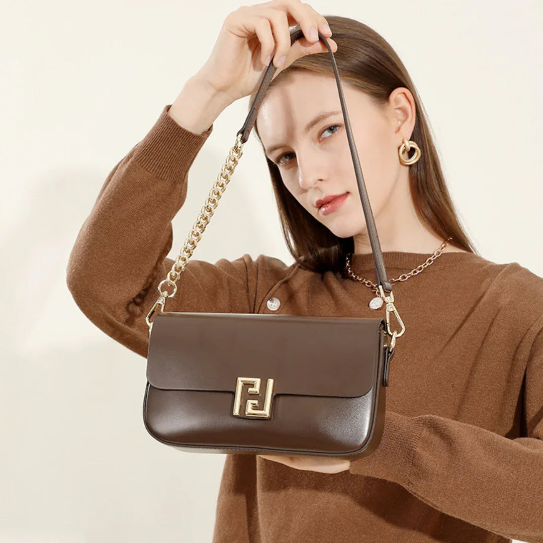 Woman in brown sweater holding brown leather shoulder bag with gold chain and logo