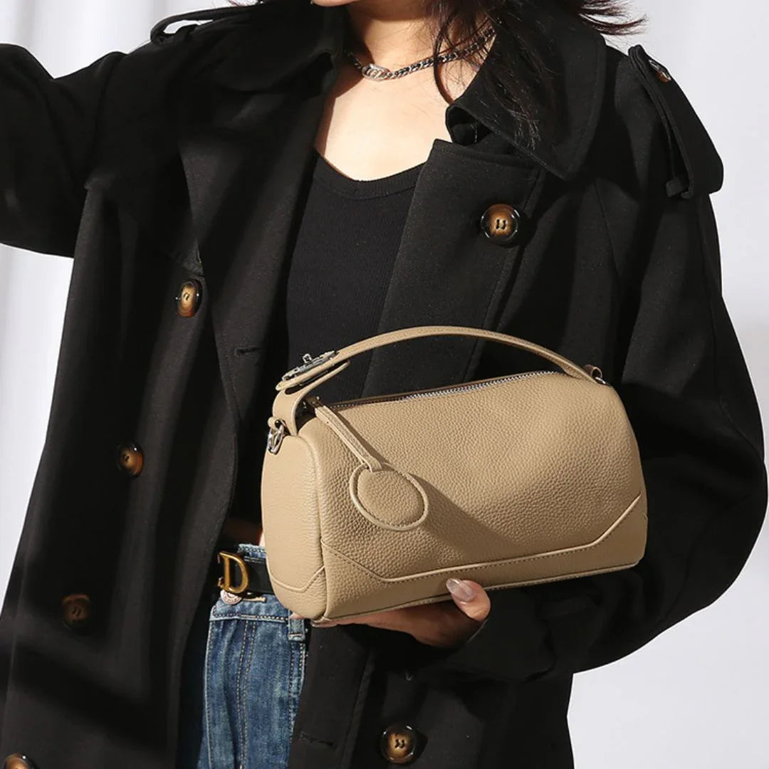 Woman in black coat holding beige leather handbag with top handle and silver zipper