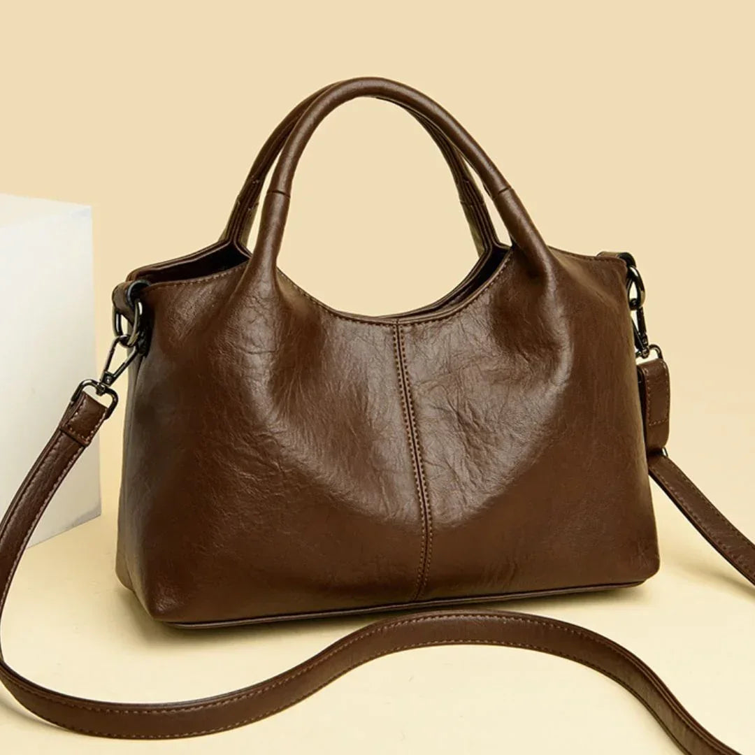 Brown leather handbag with shoulder strap on beige background