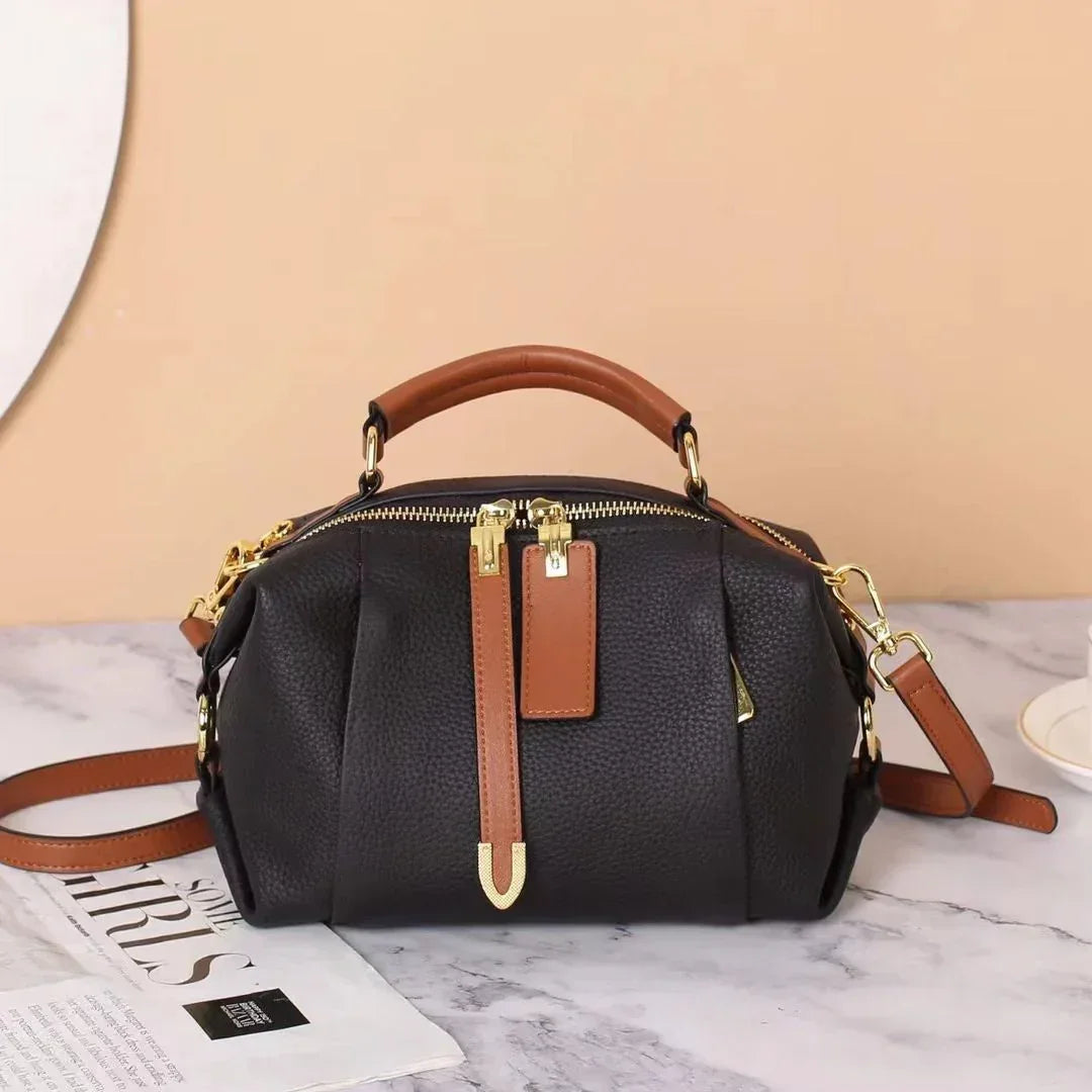 Black leather handbag with brown handles and gold hardware on a marble table