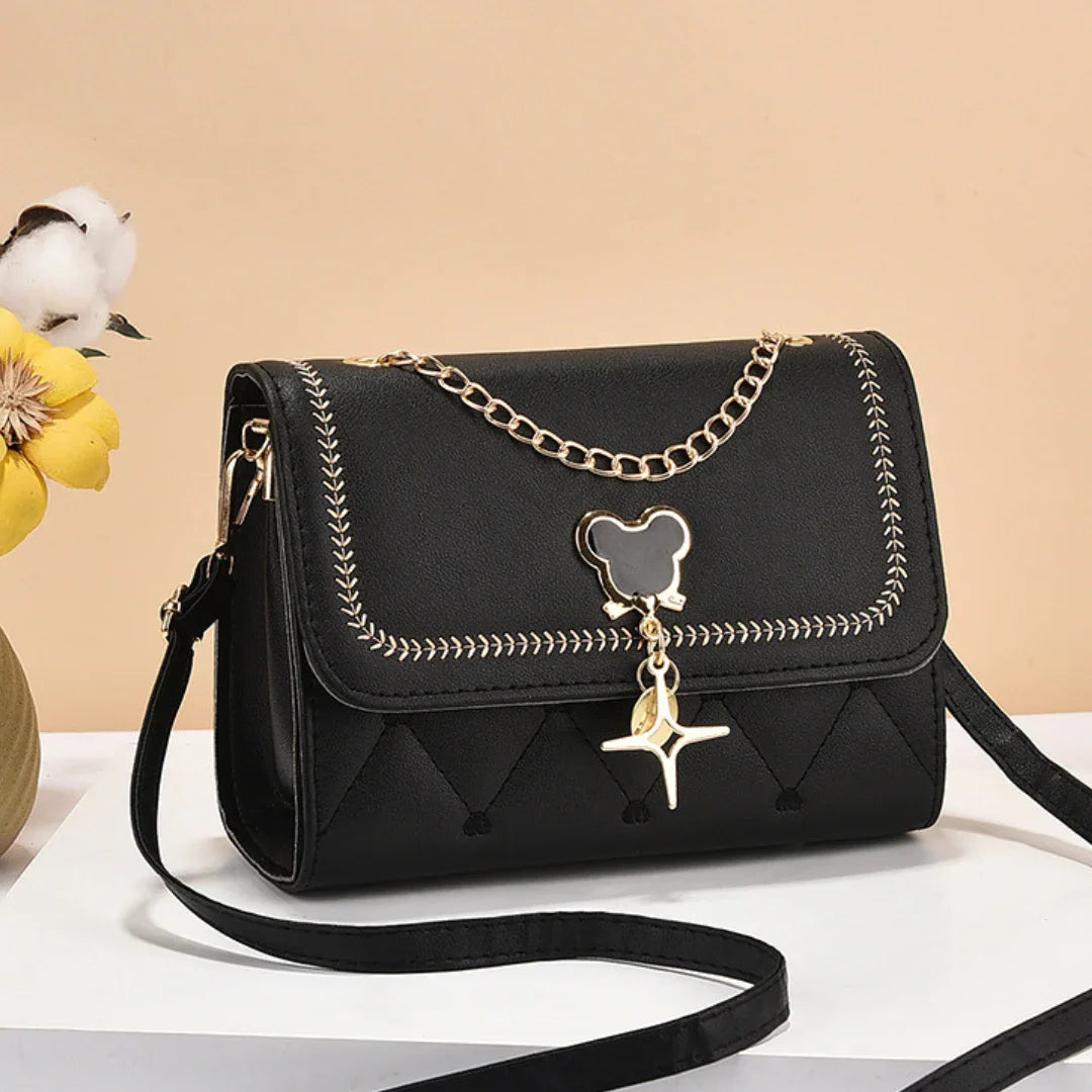 Black crossbody purse with gold chain, bear-shaped charm, and stitched detailing on display.