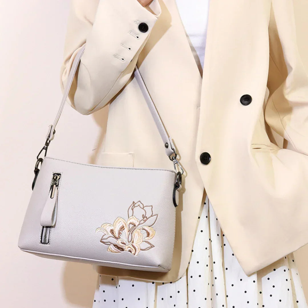 Beige handbag with floral embroidery, worn by person in cream blazer and polka dot skirt