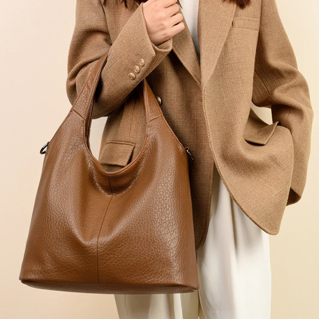 Woman in tan blazer holding large brown leather tote bag