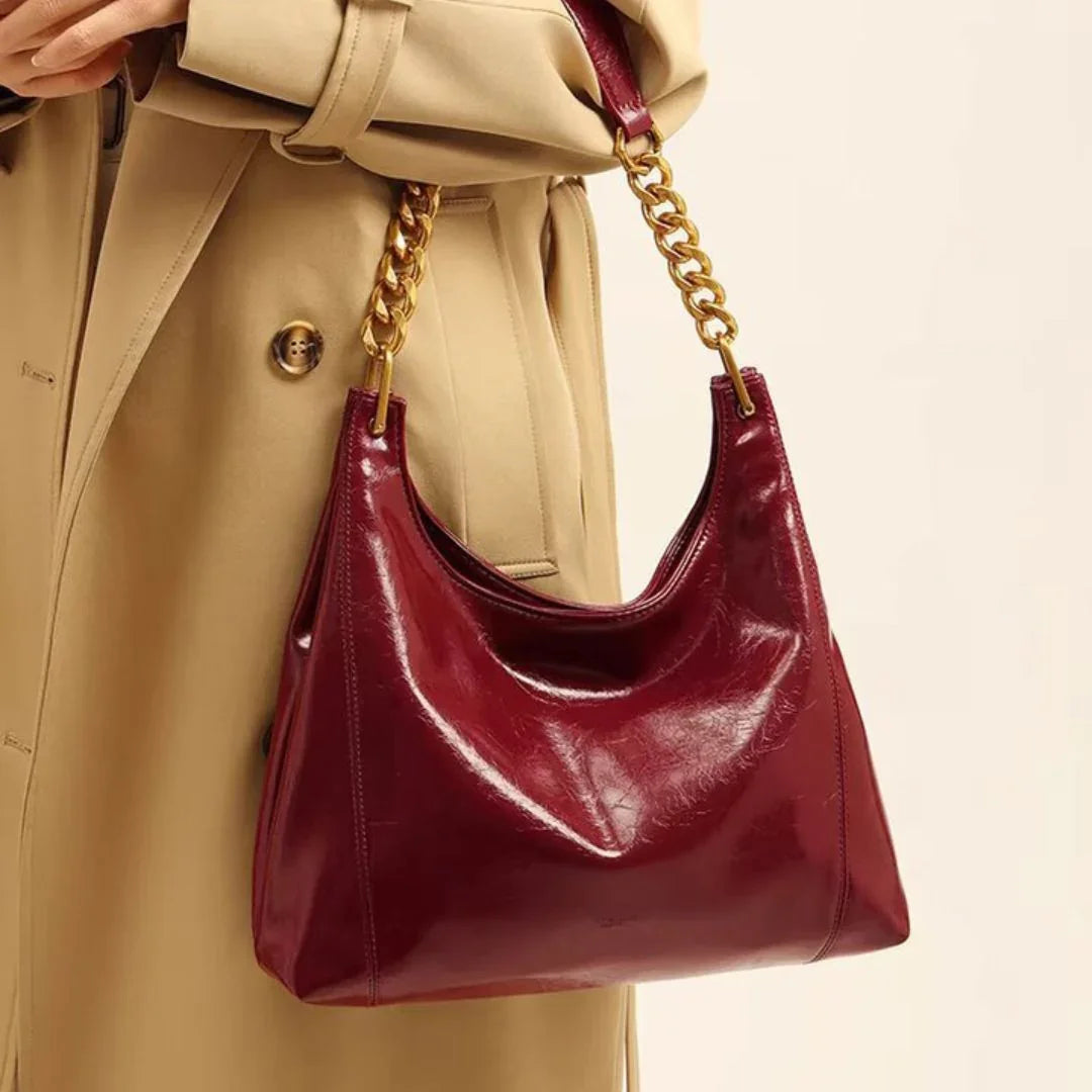 Woman wearing beige coat holding glossy burgundy leather handbag with gold chain strap