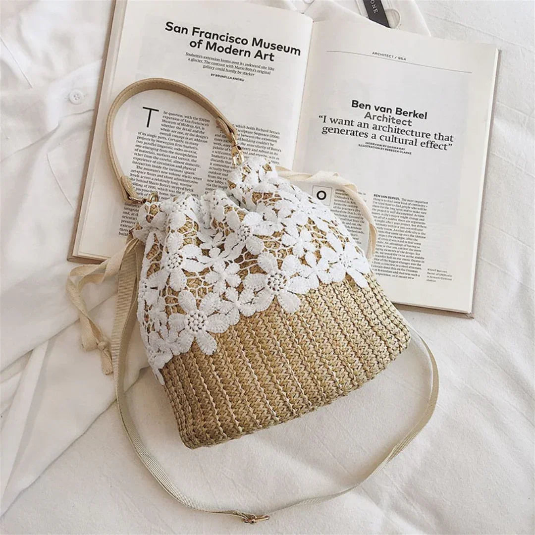 Woven straw bag with white floral lace detail on white fabric beside an open art book