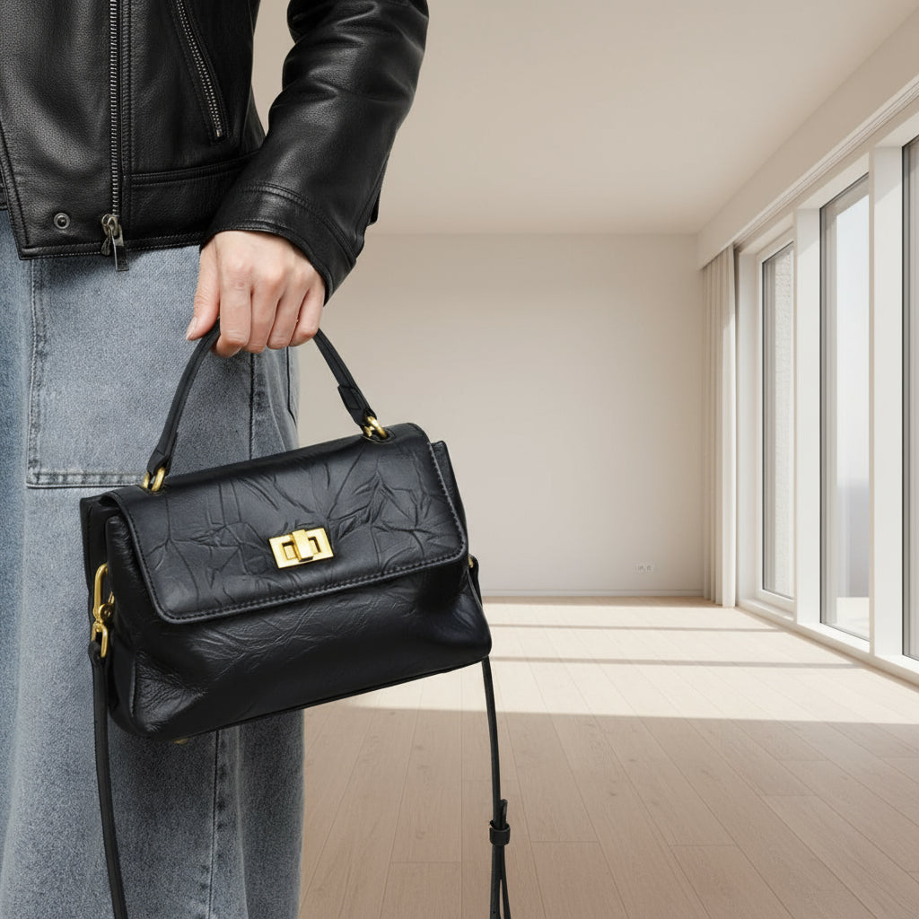 Woman holding black leather handbag with gold clasp, wearing black jacket and jeans