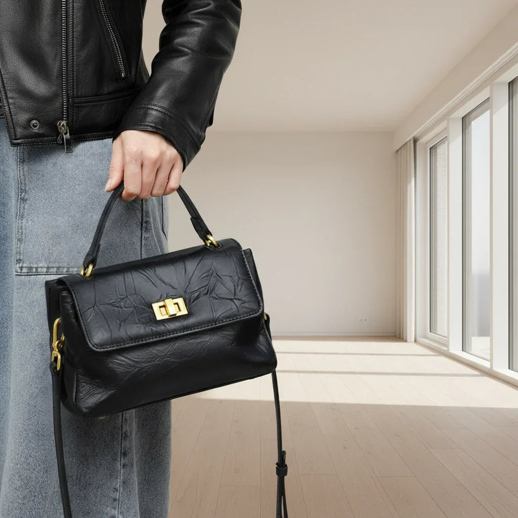 Woman holding black leather handbag with gold clasp, wearing black jacket and jeans